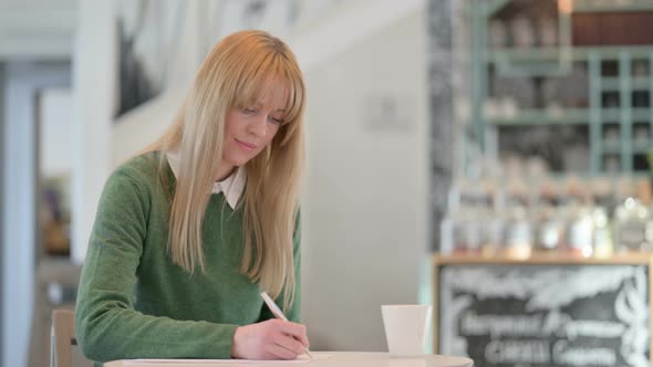 Attractive Young Woman Writing on Paper in Cafe