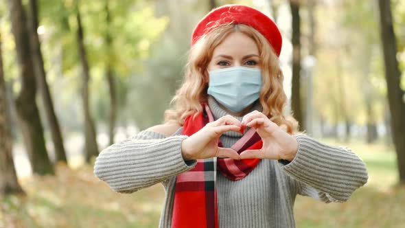 Pretty Woman in Disposable Mask Showing Heart Sign in Autumn Park