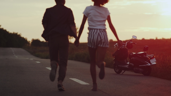 The Couple Is Smoothly All Inlove Holding Hands Running in the Sunset Towards Their Motorbike