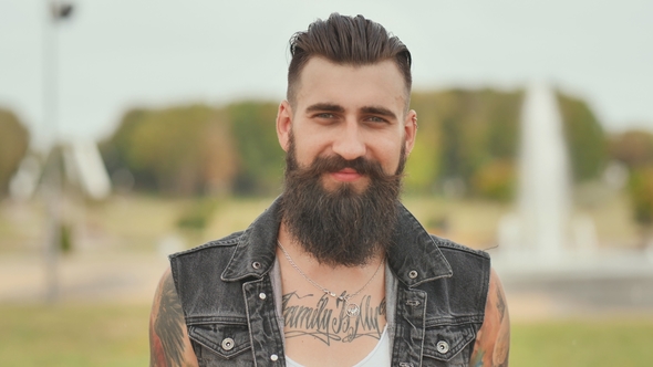 Portrait of a Brutal and Bearded Man with Tattoos on His Shoulders