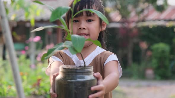 Cute little girl holding a small tree in her hand on a blurry green background in spring. earth day