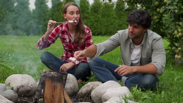 Young Couple Roasts Marshmallows on a Picnic By the Campfire