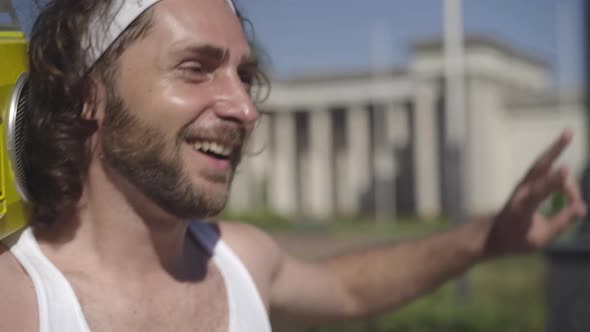 Close-up of Happy Carefree Man Walking with Retro Tape Recorder on Sunny Summer Street and Singing