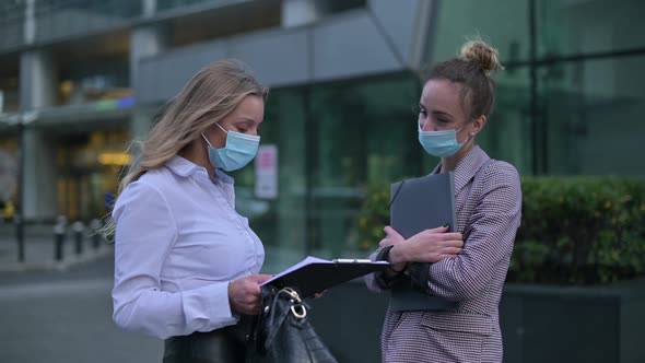 Two young business women wearing medical masks meet on the street to communicate