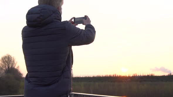 A person is taking photos with his phone while standing on a viewing platform.