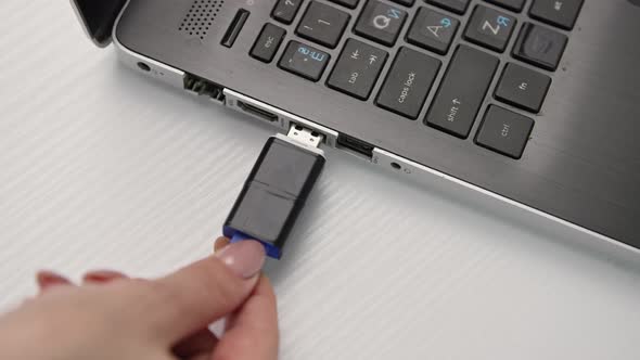 Female Hands Inserts a Flash Drive Into of a Laptop Computer on a Light Background Closeup