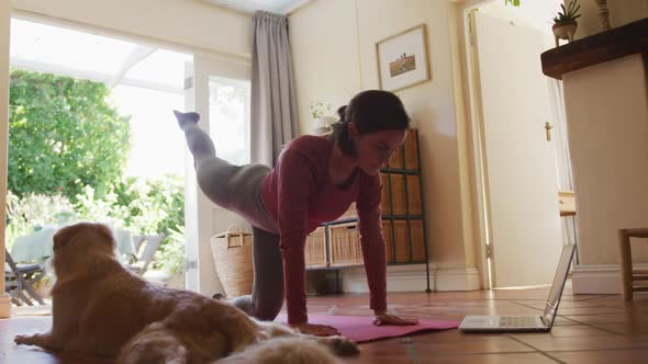 Caucasian woman exercising with her pet dog using laptop at home