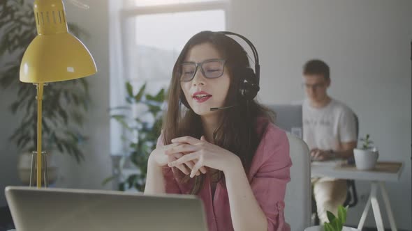 Asian Woman Operator with Headset Sittig in Front of Laptop Friendly Speaking with a Client