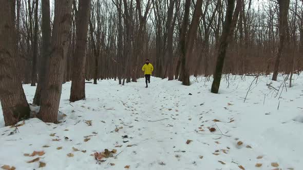 Young Fit Bearded Runner in Yellow Coat Training in Forest on Cold Winter Day