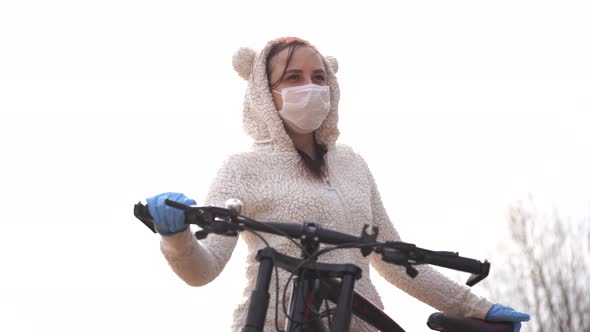 Portrait of Young Woman in Medical Mask and Gloves with Bicycle Against Sky