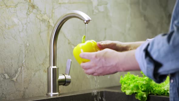 a man washes a large yellow bell pepper. cooking process by the chef. salad ingredients. caring man