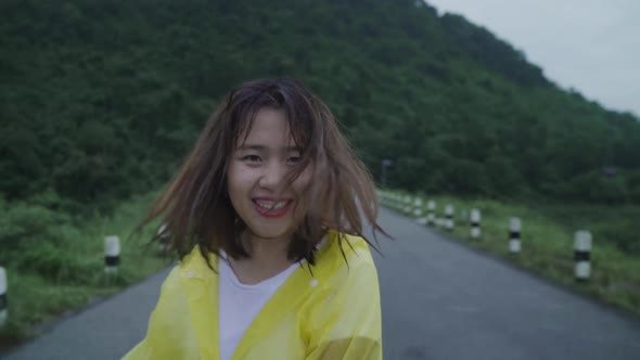 Young Asian woman feeling happy playing rain while wearing raincoat standing near lake.