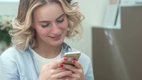 Beautiful Smiling Woman Texting on Smartphone in Beauty Salon