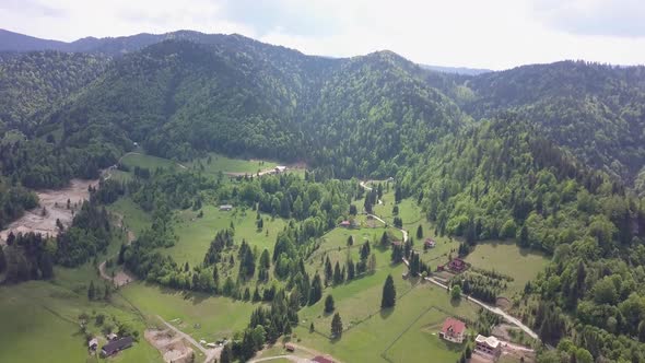 Aerial high Altitude upwards panning shot of mountain range in the distance with green woodland with