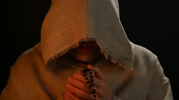 Monk in haircloth cowl robe praying in candlelight