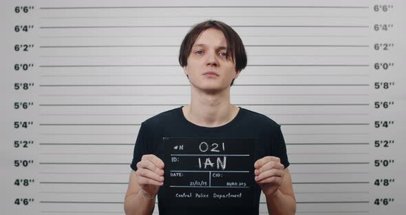 Portrait of Young Male Criminal Person Holding Sign for Photo in Police Department