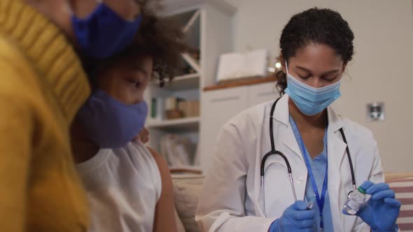 Mixed race female doctor wearing face mask making injection at home