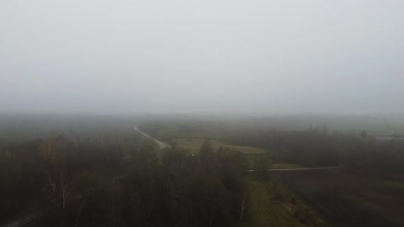 Aerial Flying through Dense Fog over Lithuanian agriculture fields and forest  on a cold autumn day