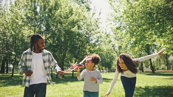 Cute Black Girl and Her Parents are Playing in the Park with a Red Plane