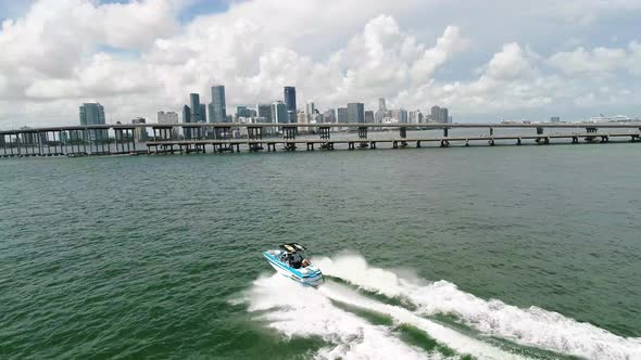 Wakeboard boat speeding across the water near a bridge with the Miami Skyline in the background