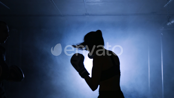 Young Woman Training with a Coach in a Boxing Club in a Smoky Gym Silhouette