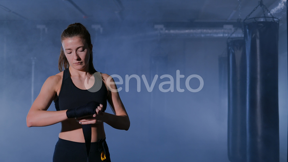 Woman Completing Wrapping of Her Hand for Boxing. In Dark Room with Smoke