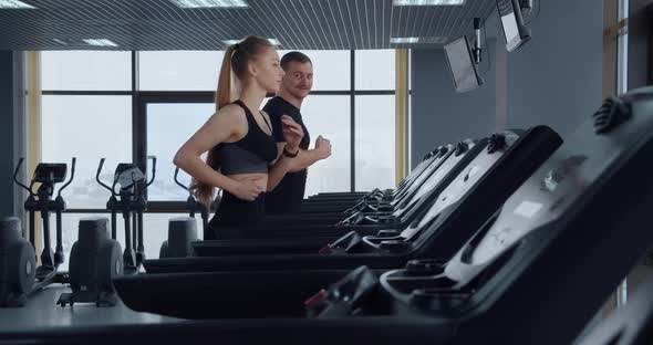 A Man And A Girl Go In For Sports In The Gym. Running On A Treadmill 