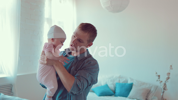 Dad Stands in a Room with a Small Baby in His Arms and Communicates with Him