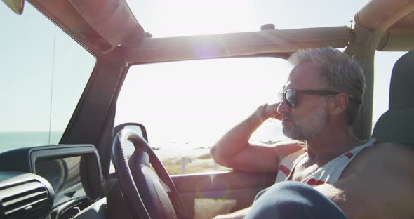 Thoughtful caucasian man in sunglasses sitting in car on sunny day by the sea