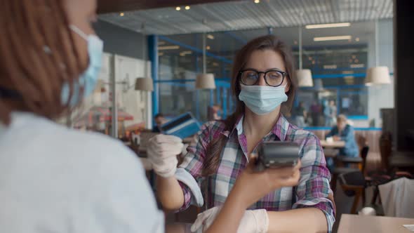 Young Female Customer in Face Mask and Gloves Making Payment Through Credit Card at Coffee Shop.