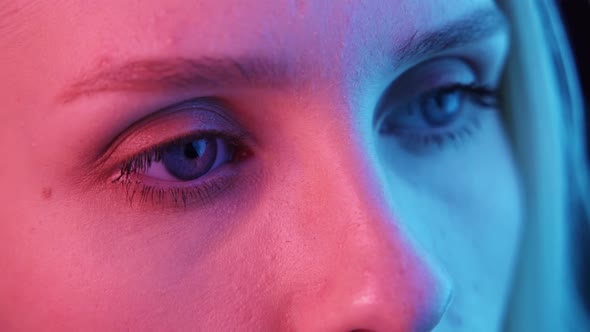 Young Woman Opens and Closes Blue Eyes Closeup in Colored Light