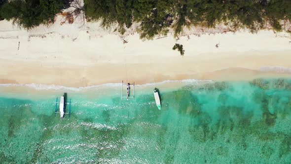 tropical island with white sandy beach and moored tour boats, aerial