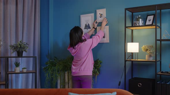 Happy Young Woman Putting Modern Picture in Frame on Blue Wall Decorating Living Room at New Home