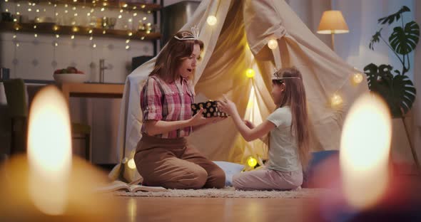 Cute Little Daughter Giving Gift Box To Mother Playing Together in Teepee Tent