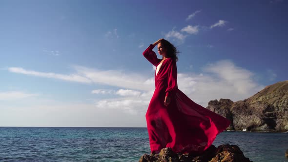 Side View a Young Beautiful Sensual Woman in a Red Long Dress Posing on a Rock High Above the Sea