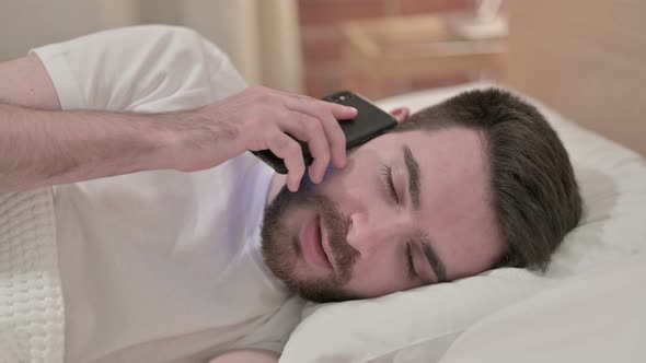 Young Man Talking on Smartphone in Bed 