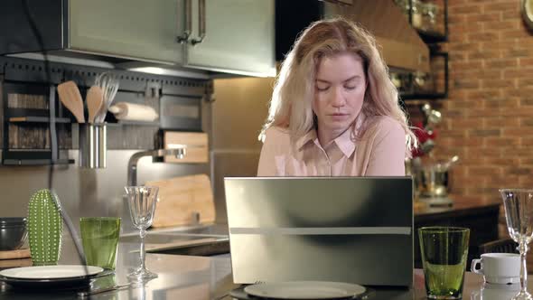 Adult Caucasian woman in kitchen goes to laptop in workplace and checks messages