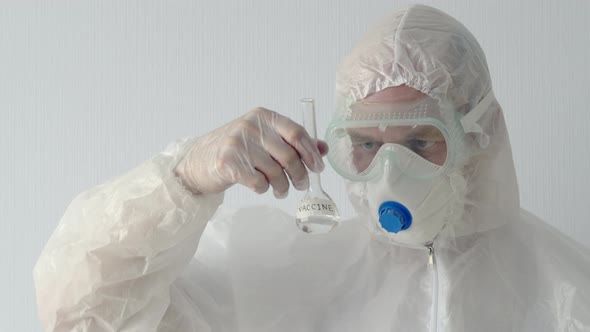 Virologist in Protective Mask and Costume Looking Vaccine Flask in Hands. Biochemist Watching