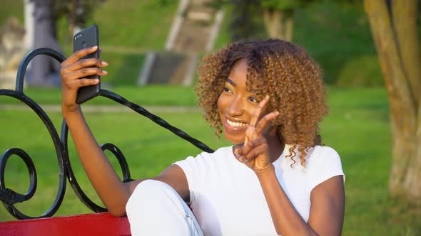 Happy African Woman Makes Selfie While Sitting on a Bench in the Park