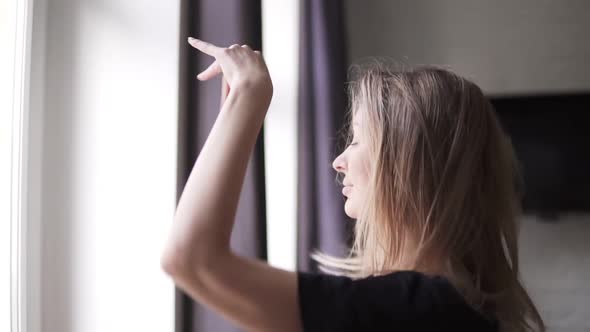 Cheerful Woman Dances Against the Background of the Large Windows of Her Apartment in the Morning
