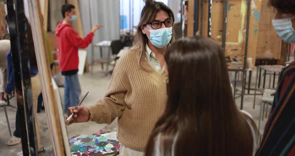 Teacher working with young students painting inside art room class wearing safety masks