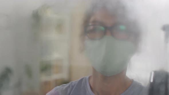Woman in Face Mask Disinfecting Glass