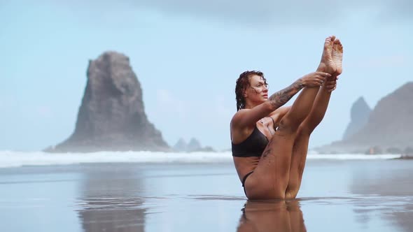 Sports Woman Training Abdominal Muscles on the Beach with Black Sand