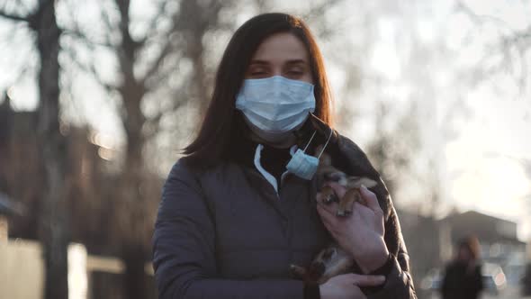 Woman in Protective Face Mask with Small Dog Wearing Medical Mask Too