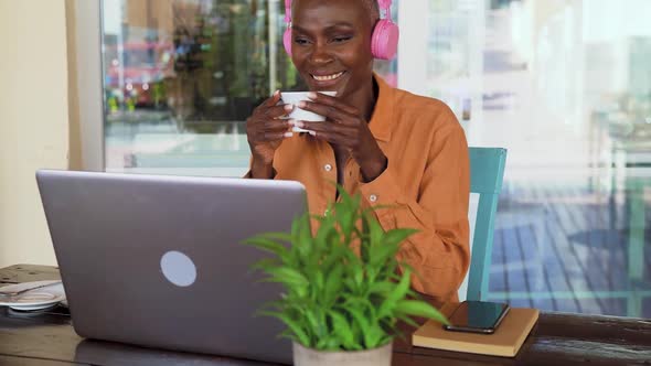 Happy Afro senior woman having fun using computer and drinking coffee in bar restaurant