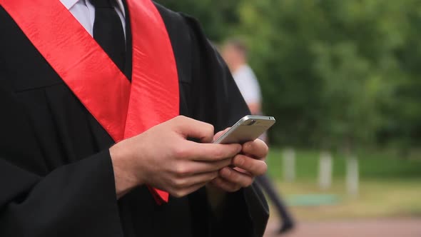 Graduate in Academic Dress Viewing Photos From Graduation Ceremony on Smartphone