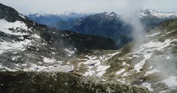 Side Aerial Top View Over Cloudy Rocky Snowy Mountain in Sunny Day with Clouds