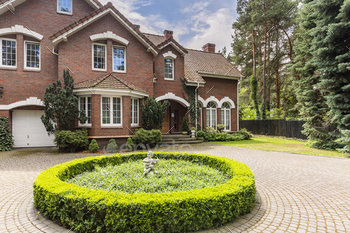 cobblestone driveway to an elegant, english style house with white windows and brick exterior