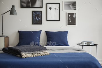 blanket. Bedside table with books and coffee next to it. Gallery of framed art on the wall. Real photo concept