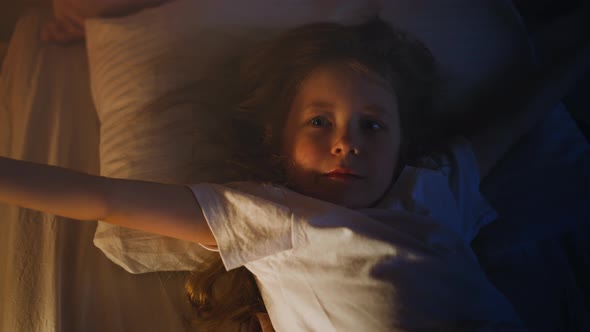 Playful Little Girl Stretches on Comfortable Bed at Night